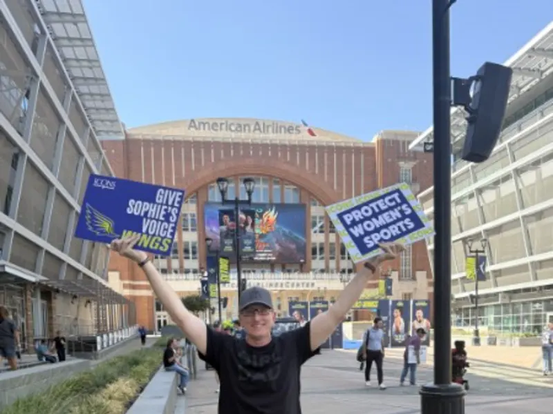 A supporter in a Girl Dad shirt raises Give Sophie’s Voice Wings and Protect Women’s Sports signs in Dallas