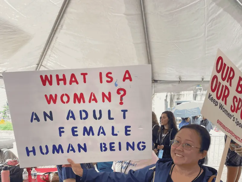 A rally-goer holds a What is a woman? An adult female human being sign