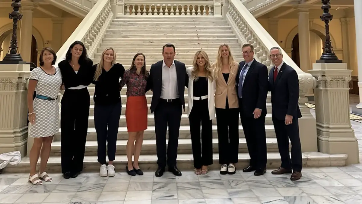 Female athletes, advocates and lawmakers on the steps inside a state capitol